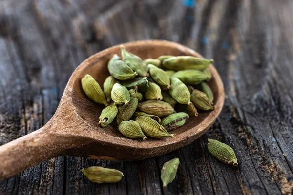 Green cardamom pods on wooden spoon